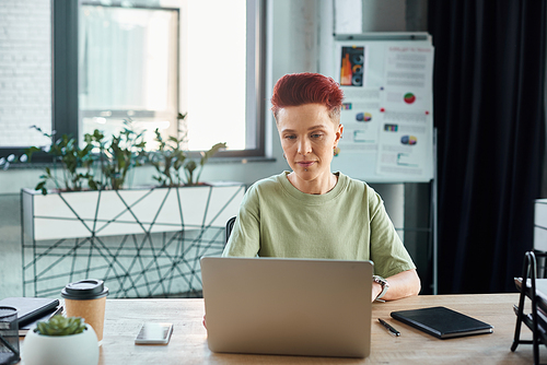 concentrated bigender manager working on laptop near coffee to go on work desk in modern office