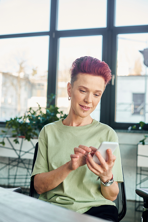 stylish non-binary individual messaging on mobile phone in contemporary modern office, business