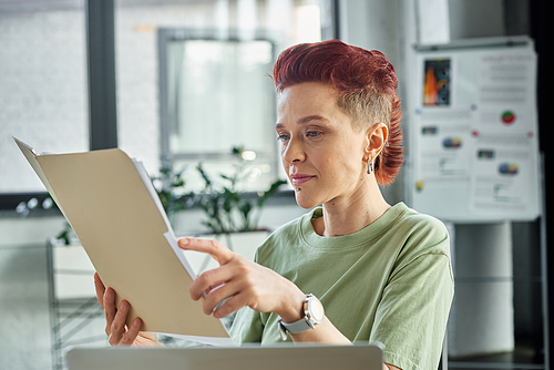 stylish queer manager in casual attire with short hair working with documents in contemporary office