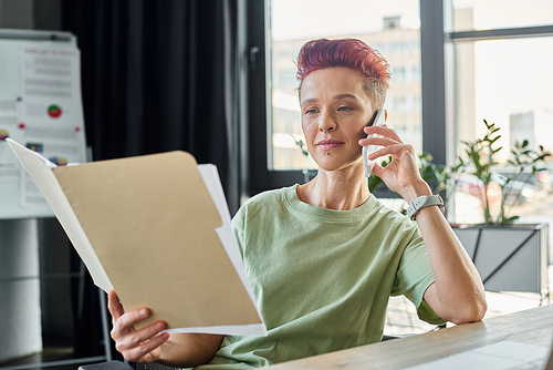 busy queer person talking on smartphone and looking at documents in modern office, multitasking