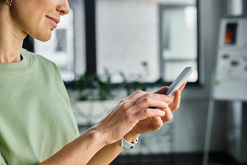 cropped view of queer manager in casual attire messaging on smartphone while standing in office