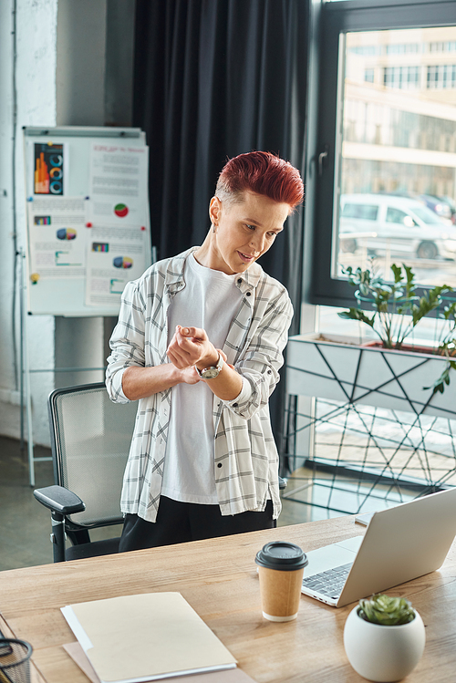 bigender manager in casual attire standing at workplace and looking at laptop in modern office