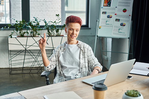 creative bigender manager sitting at workplace near laptop and showing idea sign in office