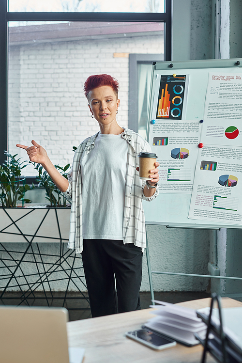 queer person with coffee to go talking near flip chart with graphs during online call on laptop