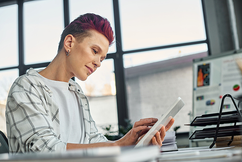 concentrated bigender person in casual attire using digital tablet while working in modern office