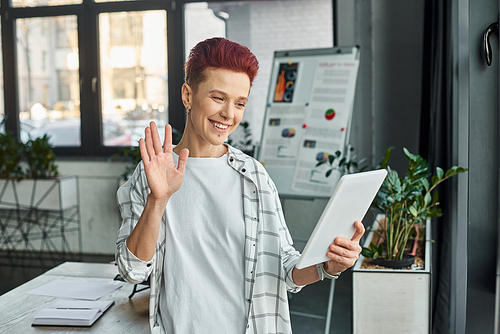 happy bigender manager waving hand during video call on digital tablet in contemporary office