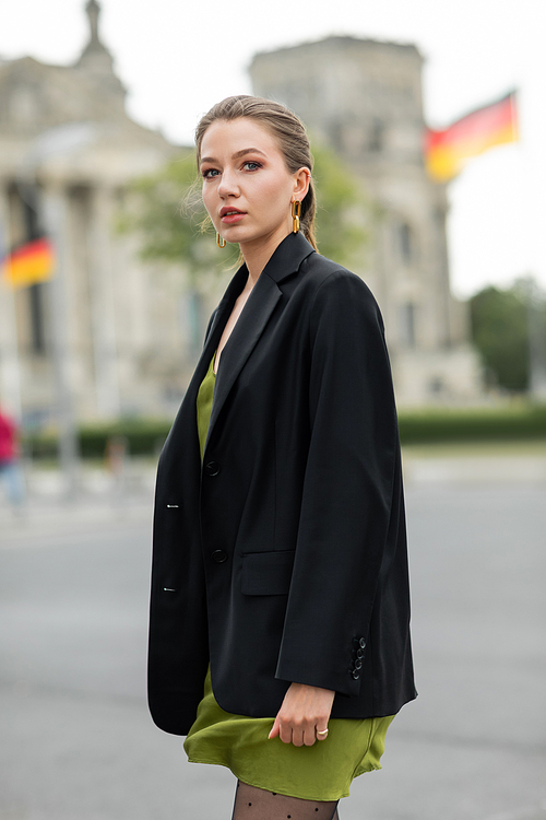 Portrait of young fair haired woman in fashionable silk dress and black jacket on street in Berlin