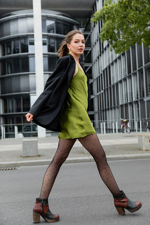 fashionable young woman in green silk dress, polka dot tights and jacket looking at camera in Berlin