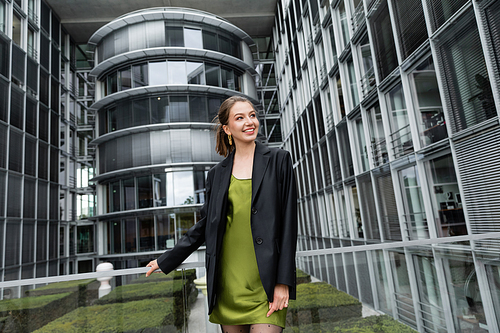 Pretty and elegant young woman in jacket and green silk dress smiling in Berlin, Germany