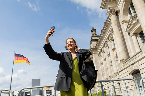 happy woman with backpack taking selfie near Reichstag Building in Berlin, Germany