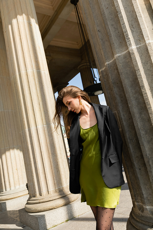 Elegant fair haired woman in green silk dress and black jacket standing in Berlin