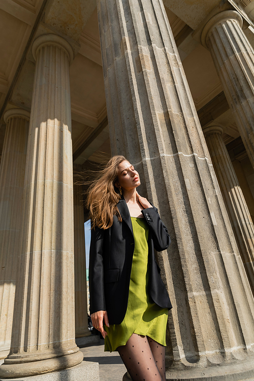 elegant and fair haired woman in black jacket and green silk dress on street in Berlin, Germany