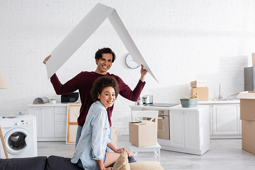 happy man holding carton roof near smiling african american girlfriend