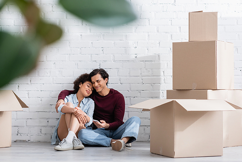 pleased multiethnic couple sitting on floor near carton boxes