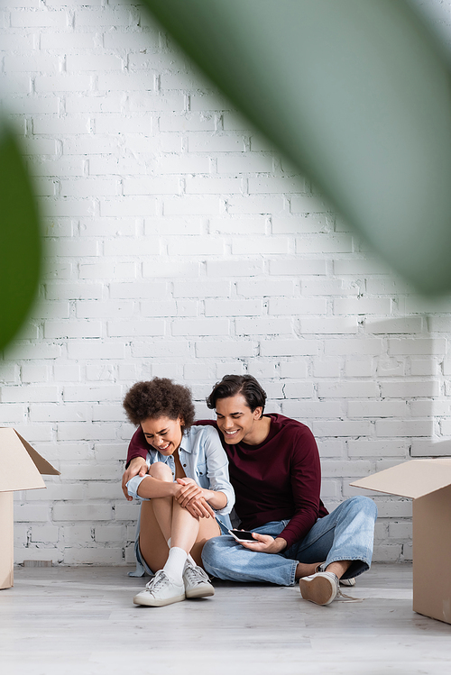 cheerful multiethnic couple sitting on floor near carton boxes