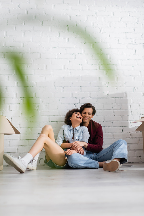 positive multiethnic couple sitting on floor near carton boxes