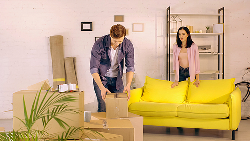 woman talking while looking at boyfriend unpacking box in new home