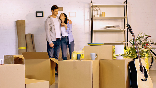 blurred man hugging pleased girlfriend near carton boxes in new home