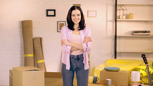 cheerful woman standing with crossed arms in new home