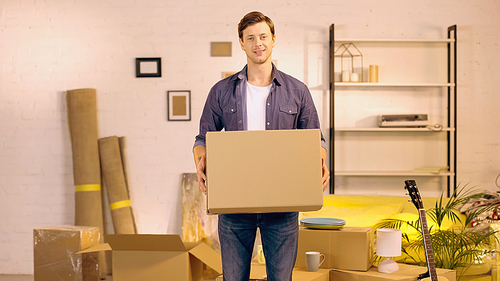 happy young man holding cardboard box in new home