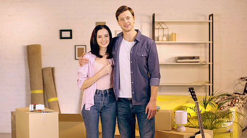 happy couple smiling and standing near boxes in new home