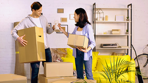 smiling man giving statuette to happy woman while standing with boxes in new home