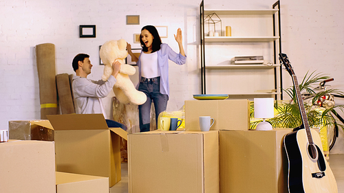 man holding teddy bear near amazed girlfriend gesturing in living room