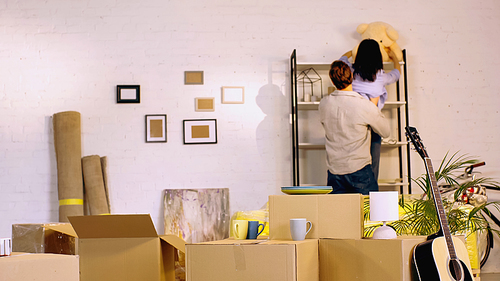 back view of couple placing teddy bear on rack in new home