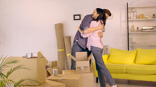 happy couple hugging near carton boxes in new home