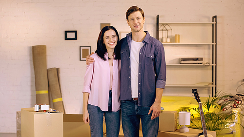 cheerful man and woman hugging while standing near boxes in new home