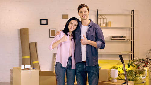 Smiling couple showing thumbs up near boxes in new home