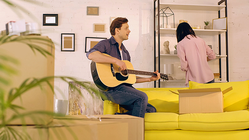 man playing acoustic guitar and singing while woman unpacking in new home