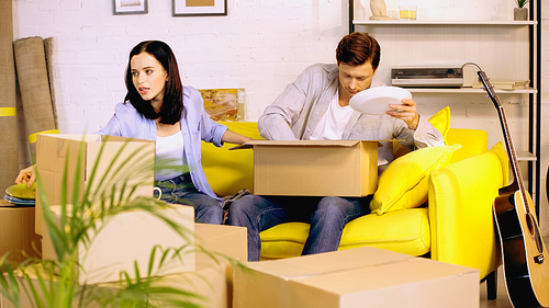 Couple packing plates in carton boxes on couch