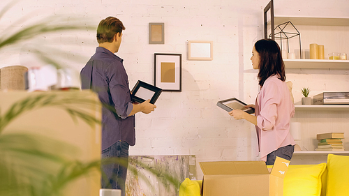 Couple holding photo frames near wall in new home