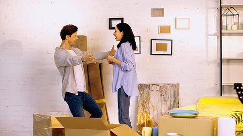 amazed woman looking at boyfriend with outstretched hands in new home