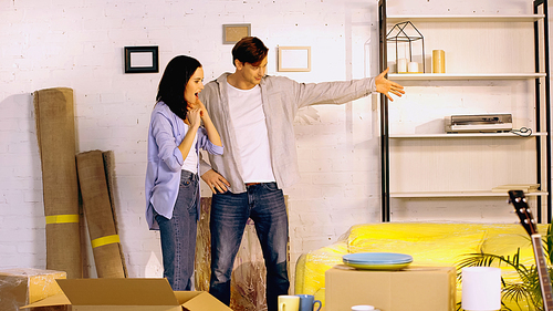 man pointing with hand at new apartment near excited girlfriend