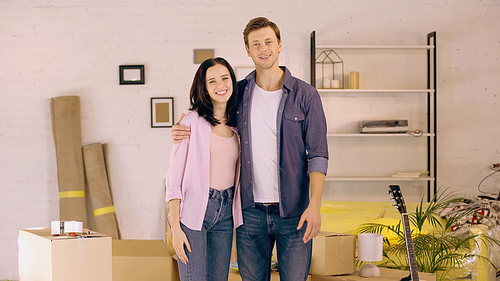 cheerful couple standing and hugging near boxes in new home