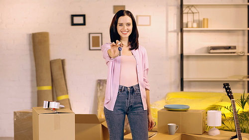 happy young woman showing keys at camera in new home