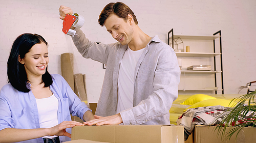 happy couple using scotch tape while packing box