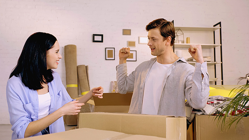 happy woman looking at boyfriend showing muscles near carton boxes