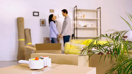 scotch tape on boxes near blurred couple holding hands in new home