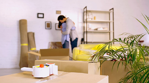 scotch tape on boxes near blurred couple hugging in new home