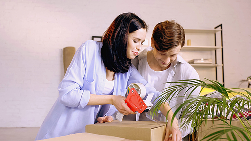 cheerful couple using scotch tape while packing box