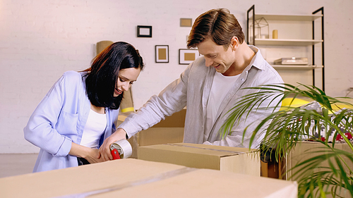 joyful couple using scotch tape while packing box