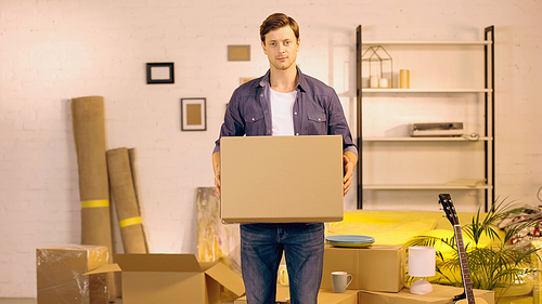 Young man holding cardboard box in new home