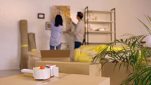 scotch tape on boxes near blurred couple hanging painting in new home