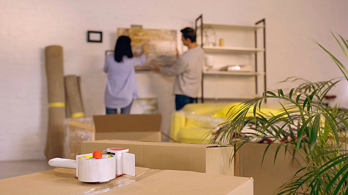 scotch tape on carton box near blurred couple hanging painting