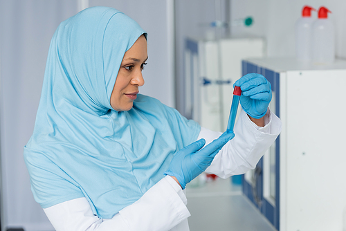 Muslim scientist in hijab and latex gloves looking at sample in test tube