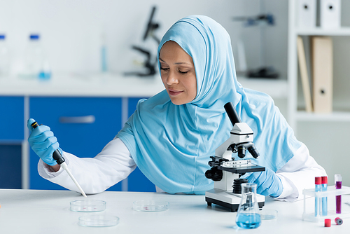 Arabian scientist working with petri dishes and pipette near microscope