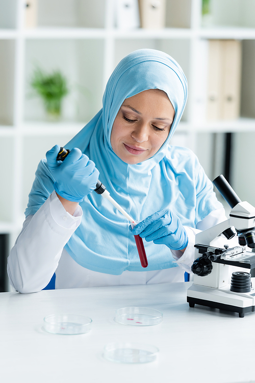 Muslim scientist working with electronic pipette and blood sample near microscope